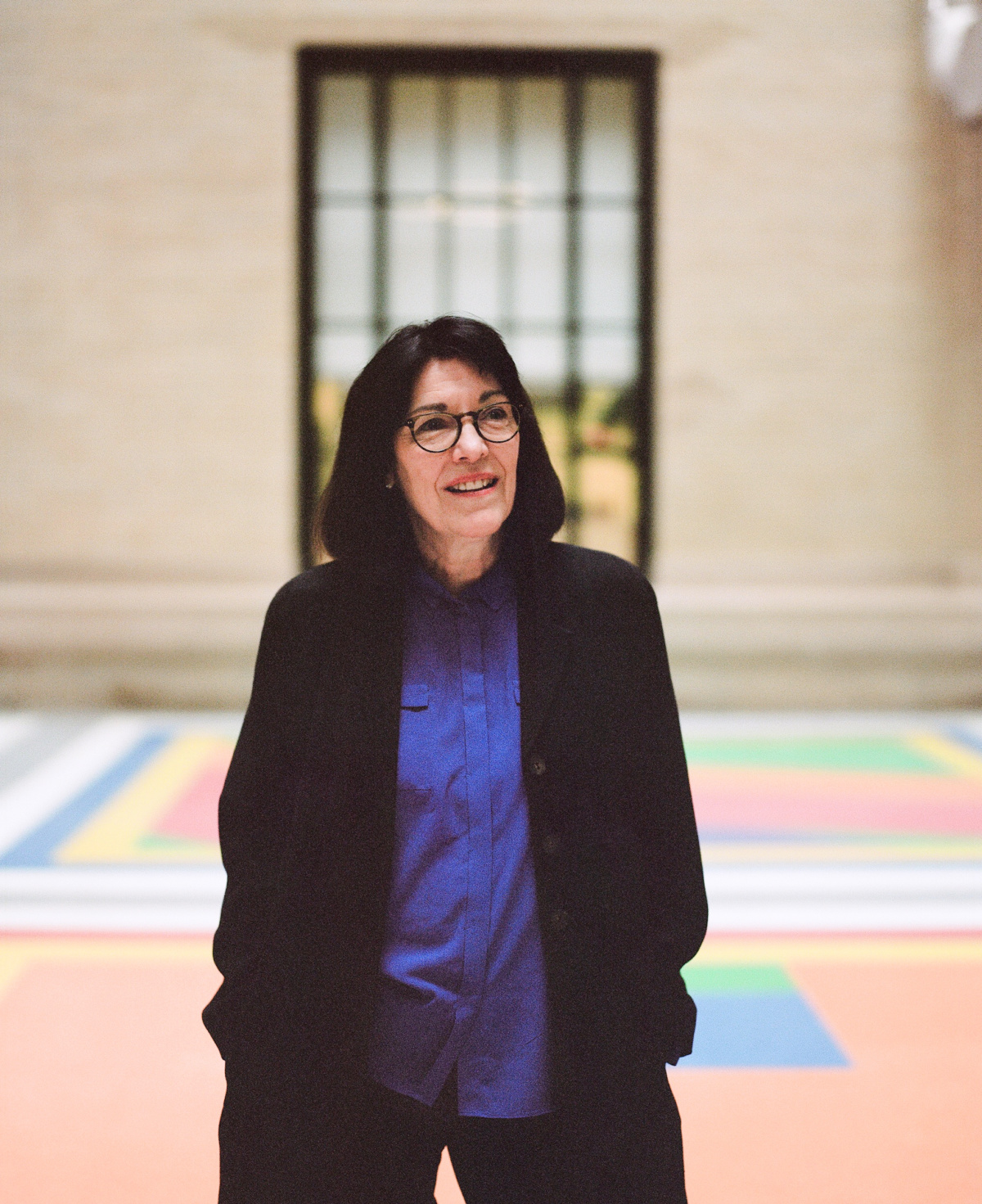 Leila Kinney stands on the colorful LeWit floor at MIT facing the camera with her hands in her pockets.